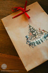 Gift bag with Christmas tree design and red ribbon on a wooden surface
