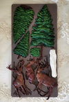 Chocolate mold with tree, deer, and rock designs on a decorative surface
