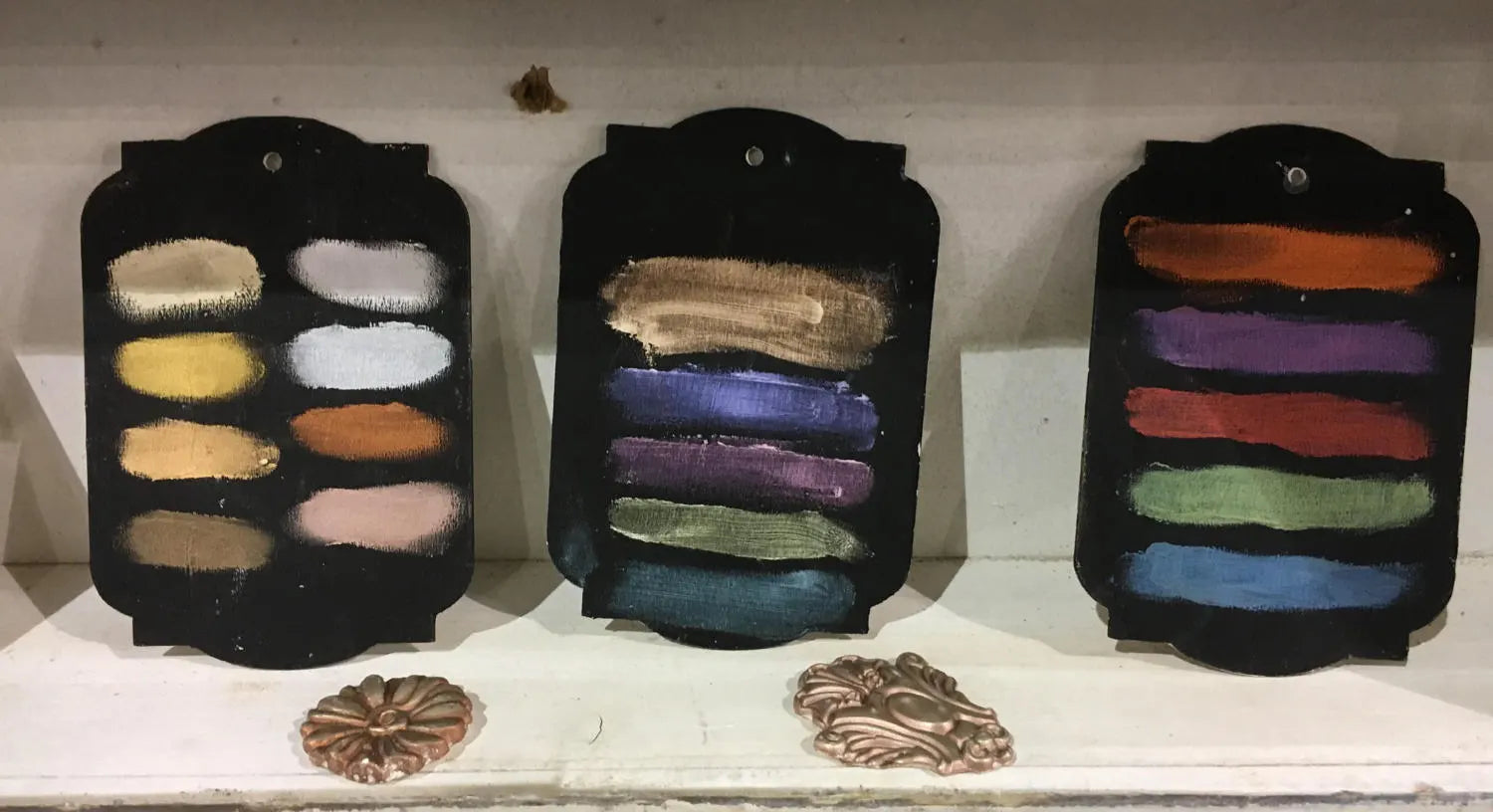 Three black wax swatches with colorful shades on a white surface.